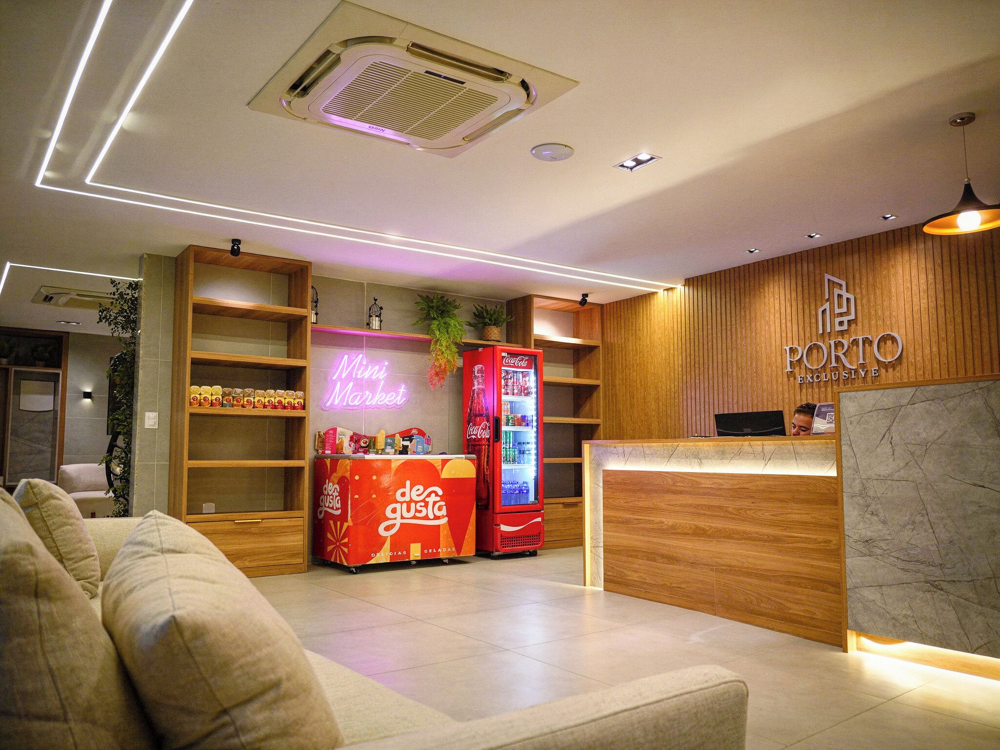 Een moderne hotellobby met een receptiebalie, een neonbord voor een minimarkt, en een Coca-Cola koelkast.