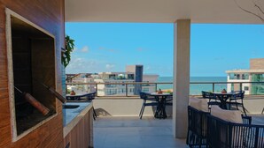 Un balcón con una parrilla, asientos exteriores y vistas al océano y edificios.