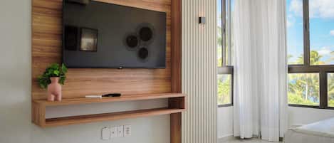 Una sala de estar moderna con un televisor de pantalla plana grande montado en una pared de madera, una pequeña planta rosa y un sofá blanco.
