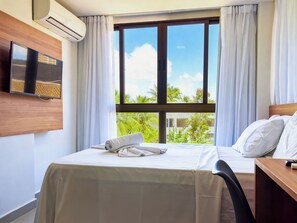 A hotel room with a bed, a desk, a TV, and a window with curtains.
