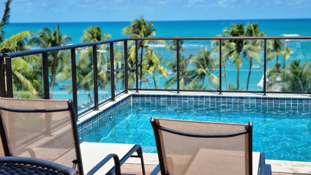 Vista a la piscina con una vista despejada del océano y palmeras.