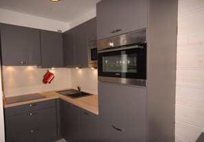 A modern kitchen with grey cabinets, a stainless steel oven, and a wooden countertop.