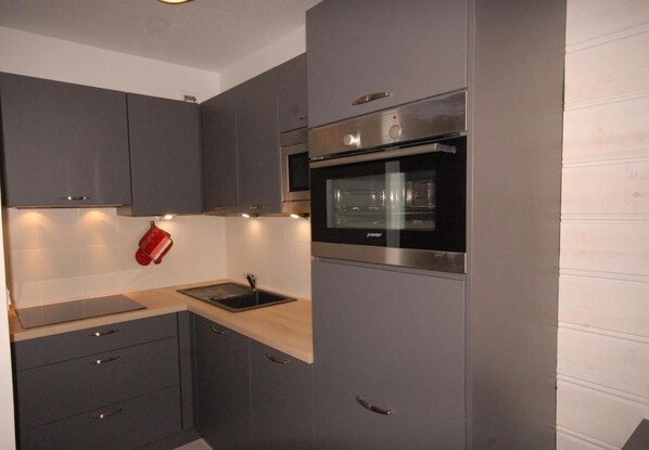 A modern kitchen with grey cabinets, a stainless steel oven, and a wooden countertop.