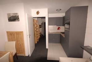 A compact kitchen with grey cabinets, a wooden door, and a small dining area with a table and chair.