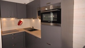 Een moderne keuken met grijze kastjes, een roestvrijstalen oven en een houten aanrecht.