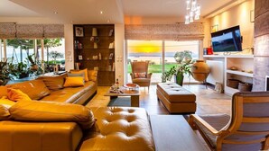 Una sala moderna con un sofá, una otomana y un sillón, una televisión y una estantería.