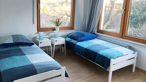 Ein Schlafzimmer mit zwei Betten, einem kleinen Tisch, einem Heizkörper und einem Fenster mit Blick auf Bäume.