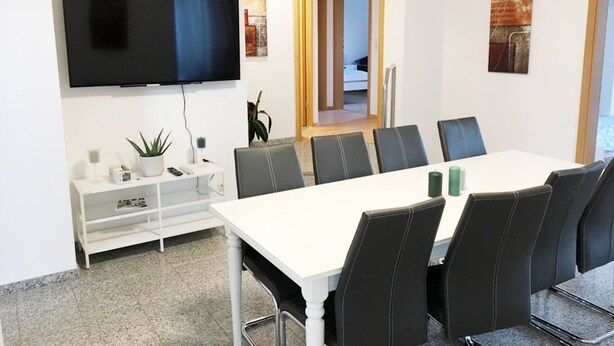 Ein Konferenzraum mit einem weißen Tisch, schwarzen Stühlen, einem Flachbildfernseher und Kunstwerken an den Wänden.