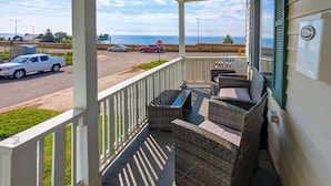 A covered porch with wicker furniture, a stop sign, and a view of the ocean. - Bayview House, Heirloom Vacations (Duluth)