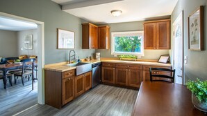 A kitchen with wooden cabinets, a stainless steel sink, and a window with a view of trees. - Bayview House, Heirloom Vacations (Duluth)