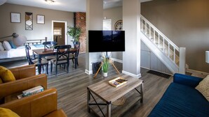 A living room with a TV, a dining area, a staircase, and a bed. - Bayview House, Heirloom Vacations (Duluth)