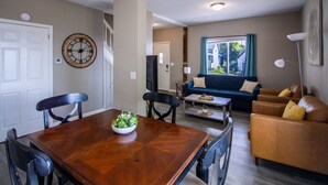 A dining area with a wooden table and chairs, a living room with a sofa and a coffee table, and a large window with curtains. - Bayview House, Heirloom Vacations (Duluth)