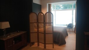 Un dormitorio con cama, escritorio, silla, lámpara y ventana con vistas a árboles.