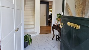 Un pasillo con piso de mármol, una escalera, un candelabro y una puerta verde con un espejo.