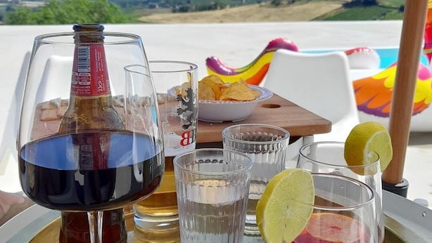 A table with a bottle of red wine, two glasses of water, and a glass with a red drink and a lime slice. - Glamping at an Agriturismo in the Vineyard (Ortezzano)