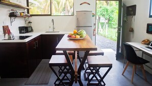 Cocina compacta con una mesa de madera, dos bancos, un refrigerador y una ventana con vistas a la vegetación.