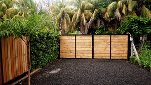 Una puerta de madera con un camino de grava que conduce a un jardín exuberante con diversas plantas y árboles.