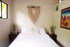 A bedroom with a bed, two bedside tables, a macrame wall hanging, and two potted plants. - Beachside private home, walk to all. Fast wifi & pet friendly. (Guanacaste)