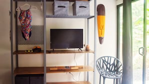 Habitación con una televisión en un estante, una silla y una ventana con vista a zonas verdes.