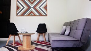 Una sala de estar moderna con un sofá gris, dos sillas negras, una mesa de centro de madera y una alfombra estampada.