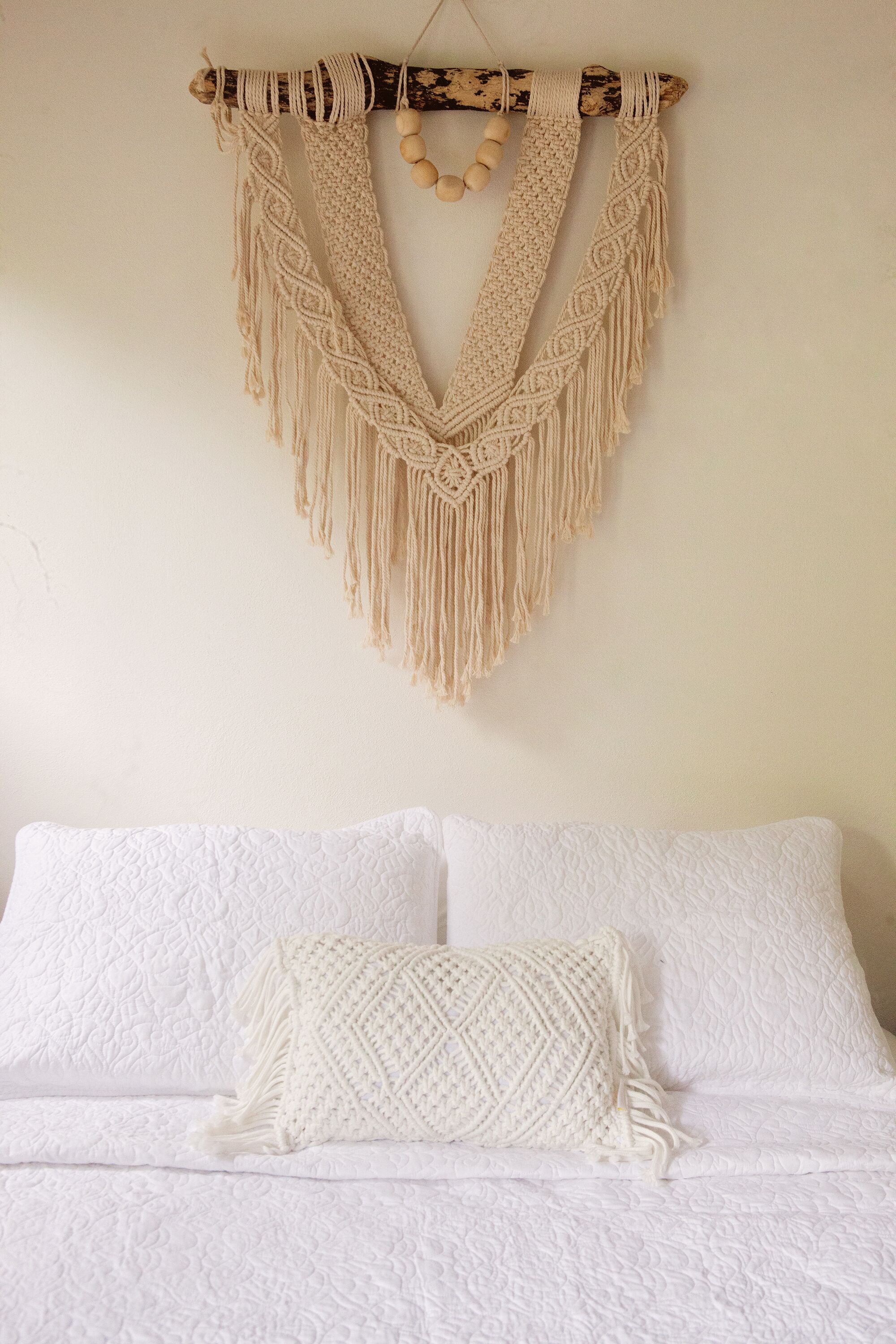 A bed with white bedding and a macramé wall hanging.