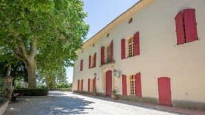 Un edificio con contraventanas rojas, una calle empedrada y un árbol grande.