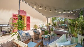 Un patio exterior con mobiliario de mimbre, una parrilla y una zona de estar cubierta.