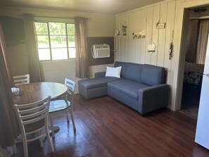 A room with a dining table, chairs, a sofa, and a refrigerator.