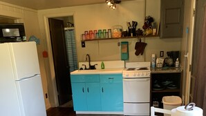 A kitchen with a wooden dining table, white chairs, a white refrigerator, a blue sink, and a stove.