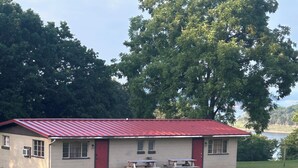 A single-story building with a red roof, two windows, and a door. There are picnic tables in front of the building.