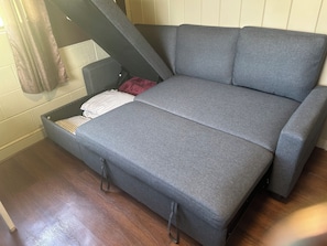 En grå bäddsoffa med en rutig kudde och en röd filt.