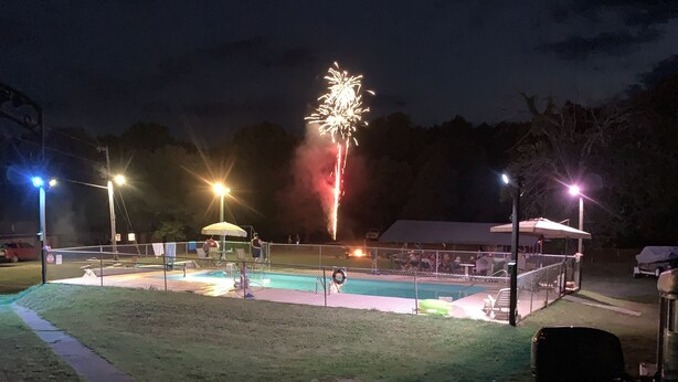 A nighttime outdoor area with a pool, seating, and a fence.
