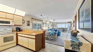 Una cocina moderna con una isla central, un comedor con mobiliario azul y un balcón con vistas.