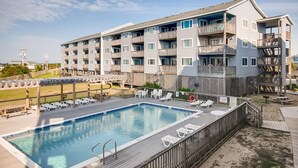 Un hotel de varios pisos con piscina, mobiliario exterior y vista al mar.