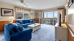 Una sala de estar con un sofá azul, una mesa de centro, un televisor y un balcón con vistas.