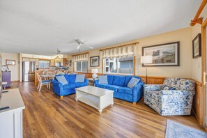 A spacious living area with a blue sofa set, a patterned armchair, and a white coffee table. - Semi-Oceanfront Condo w/ Private Balcony, Resort Pool, Elevator, Beach Boardwalk (Rodanthe)