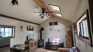 Un salon chaleureux avec un plafond en bois, une cheminée, un canapé et un coin repas comprenant une table et des chaises.