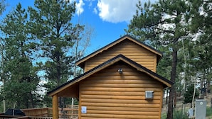 Une cabane en bois avec une allée en gravier et une terrasse délimitée par une clôture.