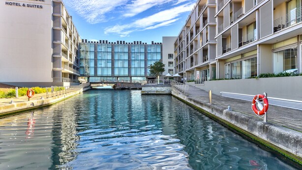 Een modern hotel met een glazen gevel, een kanaal ervoor en een drijver op het trottoir.