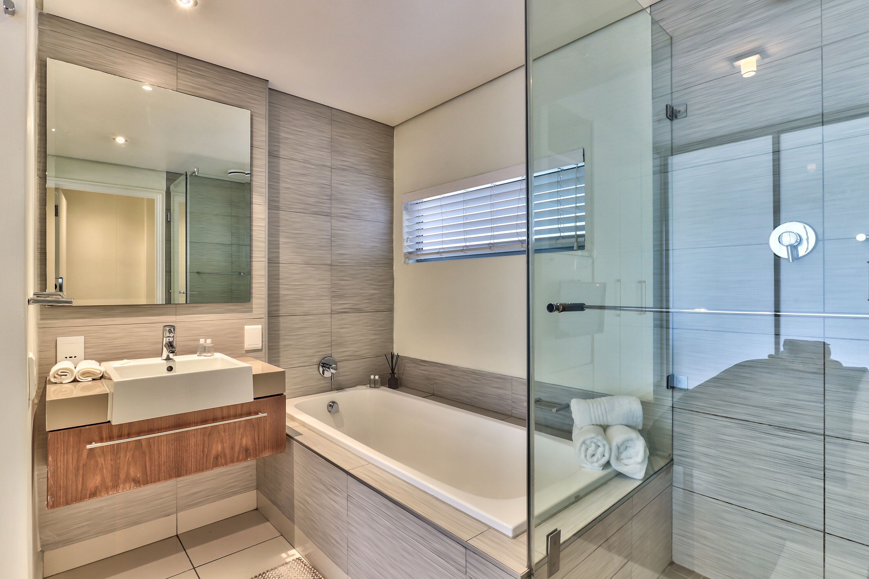 A modern bathroom with a large mirror, a bathtub, and a glass shower enclosure.