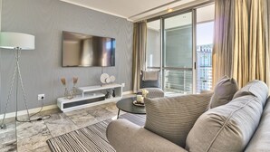 Een moderne woonkamer met een bank, een salontafel, een televisie en een balkon met gordijnen.