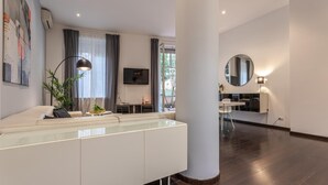 Ein modernes Wohnzimmer mit Glastisch, einer Couch, einem Fernseher und einem Essbereich mit Tisch und Stühlen.