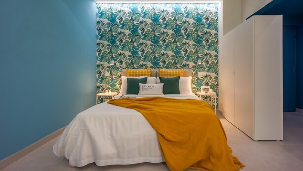 A bed with a white duvet, green and white pillows, and a mustard-colored throw blanket.