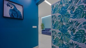 A modern interior with a blue wall, a framed artwork of a parrot, a sofa, and a wall with tropical leaf patterns.