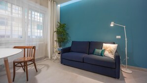 A modern living room with a blue wall, a dark blue sofa, a white table, and a wooden chair.