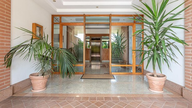 A modern entrance with glass doors, potted plants, and a tiled floor. - Kitty Apartment   to visit S. Pietro (ROMA)