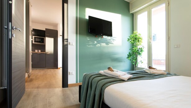 Ett modernt hotellrum med en säng, en platt-TV som är monterad på väggen, en krukväxt och utsikt över omgivningarna.