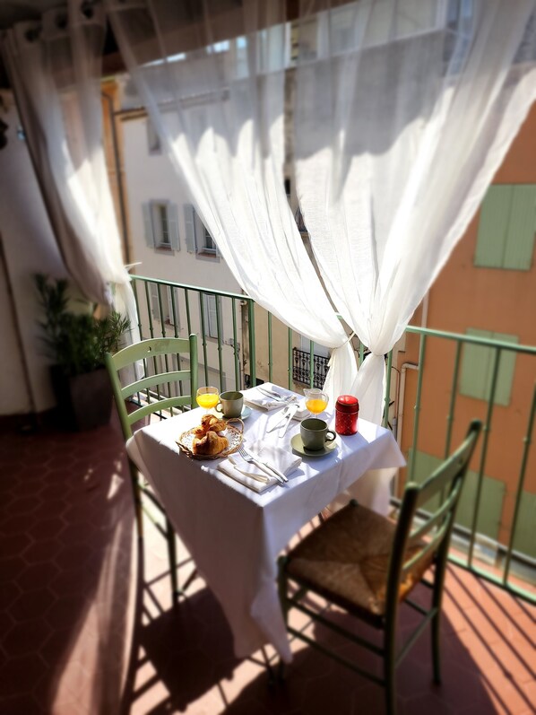 A balcony with a table set for breakfast, including croissants, orange juice, and a red mug.