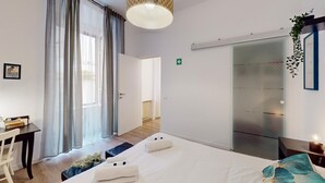 Moderni hotellihuone, jossa on suuri sänky, työpöytä ja liukuovi, joka johtaa kylpyhuoneeseen.