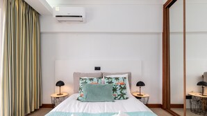 Habitación de hotel con cama, dos mesitas de noche, aire acondicionado, espejo y ventana con cortinas.